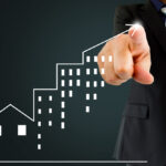 Executivo em terno aponta para gráfico de crescimento com ícones de prédios, simbolizando sucesso nos negócios imobiliários.