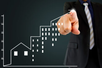 Executivo em terno aponta para gráfico de crescimento com ícones de prédios, simbolizando sucesso nos negócios imobiliários.