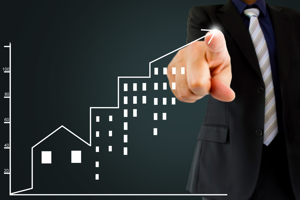 Executivo em terno aponta para gráfico de crescimento com ícones de prédios, simbolizando sucesso nos negócios imobiliários.