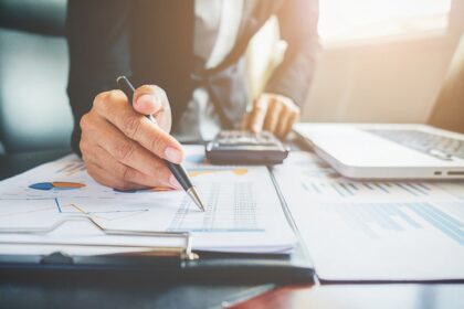 Profissional analisa gráficos e números, usando calculadora e laptop. Ambiente de escritório, foco em planejamento financeiro.
