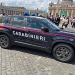 Carro da polícia Carabinieri estacionado em área histórica com turistas ao fundo, em frente a uma catedral imponente.