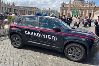 Carro da polícia Carabinieri estacionado em área histórica com turistas ao fundo, em frente a uma catedral imponente.