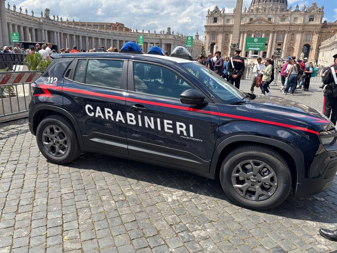 Carro da polícia Carabinieri estacionado em área histórica com turistas ao fundo, em frente a uma catedral imponente.