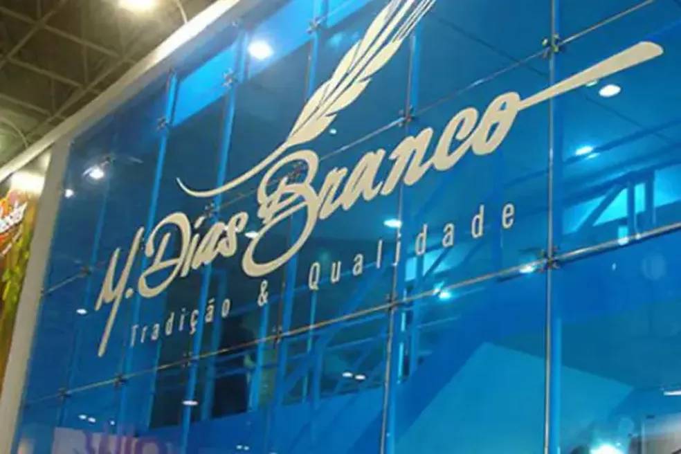 Fachada azul com logotipo e slogan da empresa M. Dias Branco em destaque, representando tradição e qualidade.