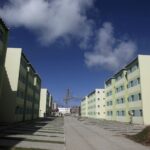 Conjunto habitacional com prédios residenciais em tons de verde, céu azul, e uma grua ao fundo.