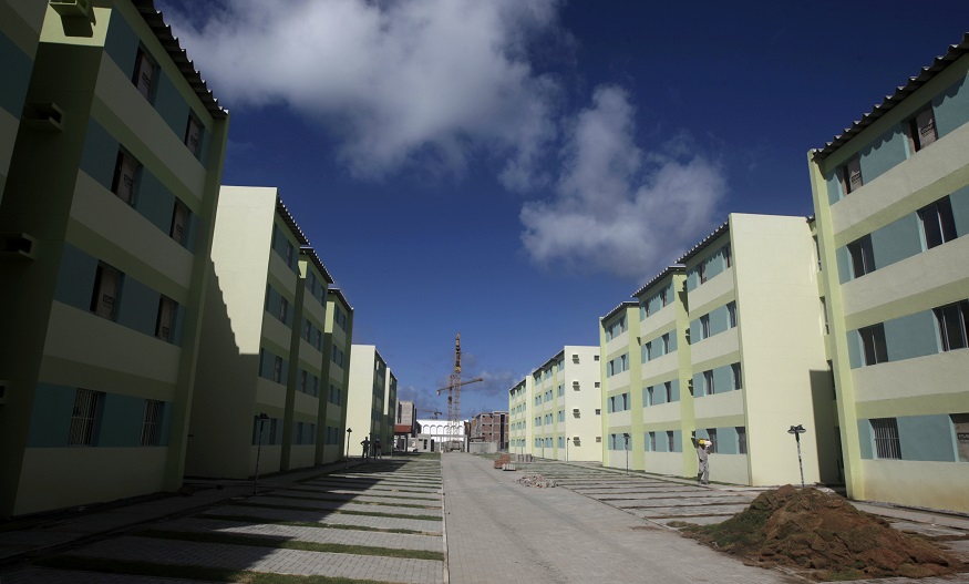 Conjunto habitacional com prédios residenciais em tons de verde, céu azul, e uma grua ao fundo.