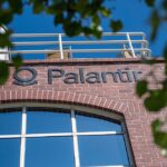 Fachada de tijolos vermelhos com logo da Palantir, destacada por arquitetura moderna e janelas amplas.