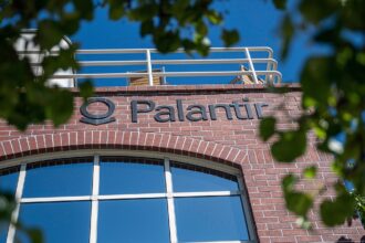 Fachada de tijolos vermelhos com logo da Palantir, destacada por arquitetura moderna e janelas amplas.