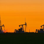 Bombas de petróleo operando em campo ao pôr do sol, realçando a indústria de energia em um cenário de céu alaranjado.