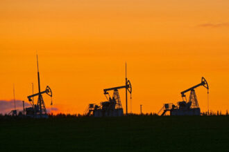 Bombas de petróleo operando em campo ao pôr do sol, realçando a indústria de energia em um cenário de céu alaranjado.