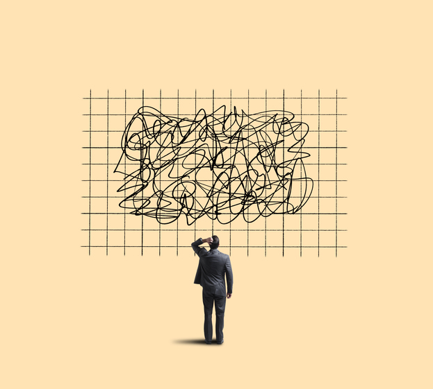 Homem de negócios confuso observa quadro com rabiscos desordenados, simbolizando complexidade e desafios no trabalho.