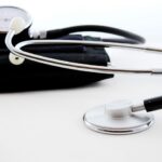 Estetoscópio prateado e aparelho de pressão preto em fundo branco, representando ferramentas de saúde e diagnóstico médico.