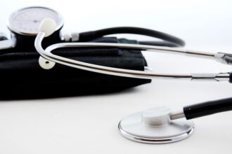 Estetoscópio prateado e aparelho de pressão preto em fundo branco, representando ferramentas de saúde e diagnóstico médico.