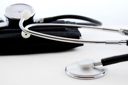 Estetoscópio prateado e aparelho de pressão preto em fundo branco, representando ferramentas de saúde e diagnóstico médico.