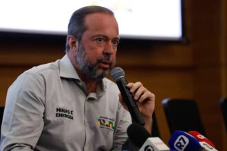 Homem segura microfone durante coletiva de imprensa sobre tema de energia, com camisas identificando Minas e Energia.
