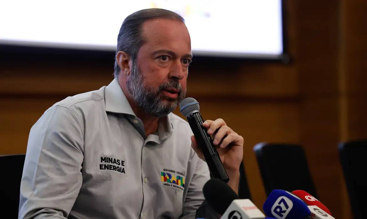 Homem segura microfone durante coletiva de imprensa sobre tema de energia, com camisas identificando Minas e Energia.