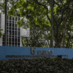 Entrada da Sabesp em São Paulo, cercada por árvores. Fachada moderna com placa azul destacando o nome da companhia.