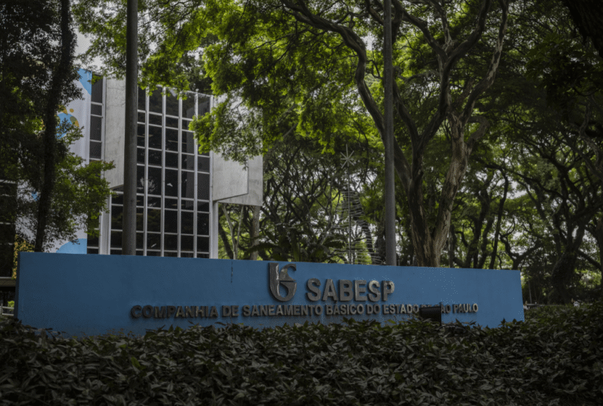 Entrada da Sabesp em São Paulo, cercada por árvores. Fachada moderna com placa azul destacando o nome da companhia.