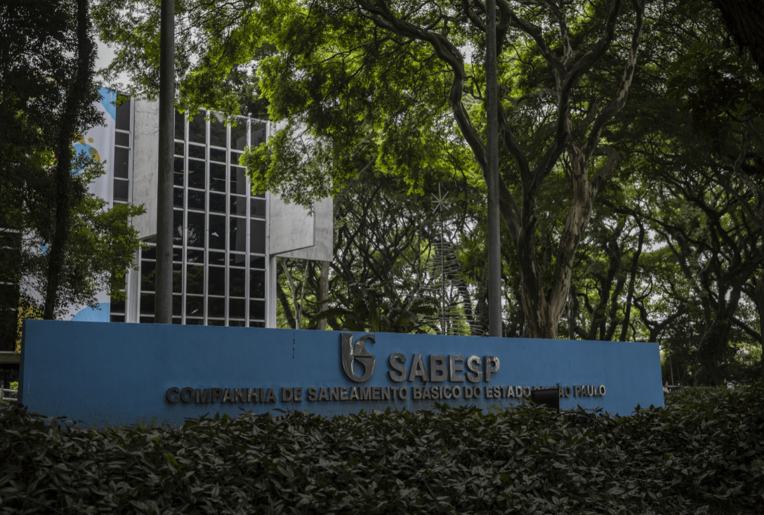 Entrada da Sabesp em São Paulo, cercada por árvores. Fachada moderna com placa azul destacando o nome da companhia.