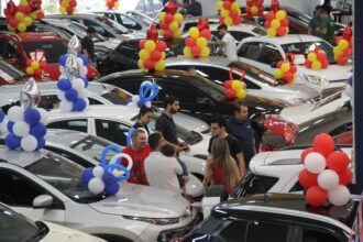 Feira de carros com várias pessoas examinando veículos decorados com balões coloridos, destacando oferta e negociação.