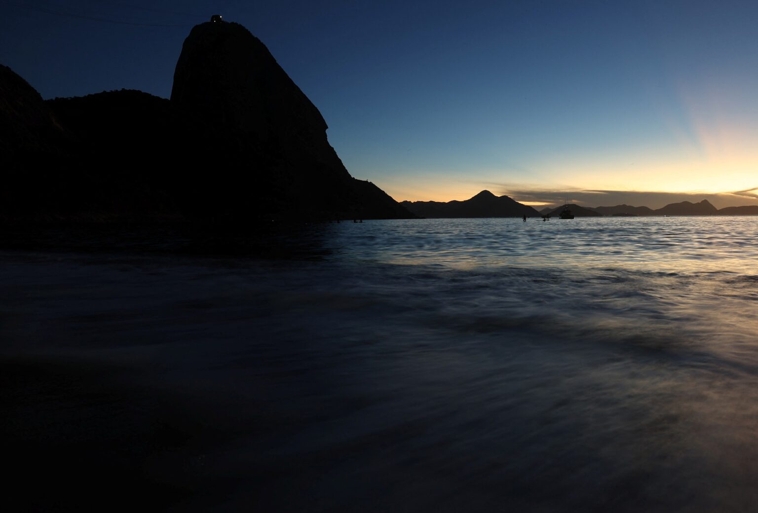 Pôr do sol no Rio de Janeiro, com o Pão de Açúcar em silhueta e o mar refletindo a luz suave do entardecer.
