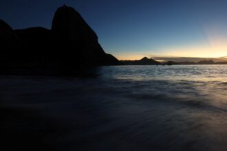 Pôr do sol no Rio de Janeiro, com o Pão de Açúcar em silhueta e o mar refletindo a luz suave do entardecer.