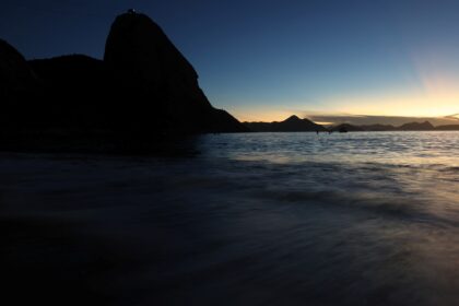 Pôr do sol no Rio de Janeiro, com o Pão de Açúcar em silhueta e o mar refletindo a luz suave do entardecer.