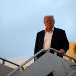 Homem descendo escada de avião presidencial, com o selo dos Estados Unidos ao fundo, sob céu azul claro.