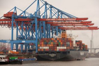 Navio de carga no Terminal de Contêineres de Altenwerder, cercado por guindastes azuis e vermelhos, movimentando contêineres coloridos.