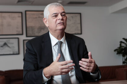 Eletrobras muda nome para Axia Energia em 22 de outubro Um homem de terno preto e gravata cinza está sentado em uma mesa, gesticulando com as mãos enquanto fala. Ele tem cabelo grisalho e uma expressão séria. Ao fundo, há quadros com desenhos ou gráficos nas paredes e uma planta em um canto. O ambiente parece ser um escritório moderno.