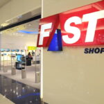 A imagem mostra a entrada de uma loja chamada Fast Shop, com um grande letreiro em destaque. O letreiro é composto pelas palavras