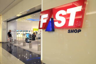 A imagem mostra a entrada de uma loja chamada Fast Shop, com um grande letreiro em destaque. O letreiro é composto pelas palavras