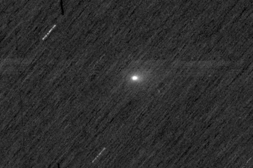 Cometa com núcleo brilhante e cauda difusa visível no centro da imagem, sobre fundo escuro pontilhado por estrelas desfocadas e traços de movimento.