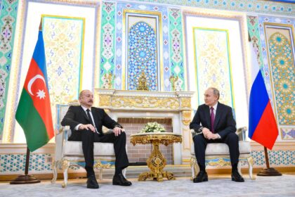 Presidente do Azerbaijão e presidente da Rússia sentados em cadeiras elegantes em sala decorada com padrões geométricos e florais. Bandeiras do Azerbaijão e da Rússia posicionadas ao lado de cada líder, com mesa dourada e arranjo floral entre eles.
