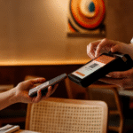 Pessoa faz pagamento por aproximação em restaurante, aproximando o celular de uma maquininha de cartão segurada por um garçom.