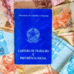 Pagamento da primeira parcela do 13º salário em 2025 Fotografia de uma CLT sobre notas de real para ilustrar matérias sobre 13º salário, crédito consignado, direitos trabalhistas