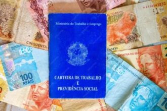 Fotografia de uma CLT sobre notas de real para ilustrar matérias sobre 13º salário, crédito consignado, direitos trabalhistas