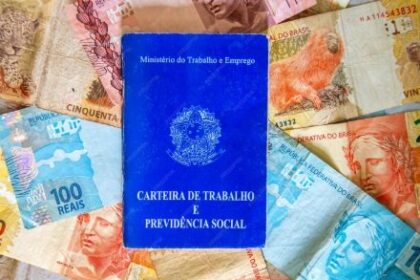 Pagamento da primeira parcela do 13º salário em 2025 Fotografia de uma CLT sobre notas de real para ilustrar matérias sobre 13º salário, crédito consignado, direitos trabalhistas