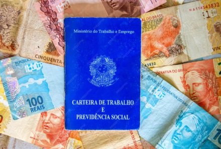 Pagamento da primeira parcela do 13º salário em 2025 Fotografia de uma CLT sobre notas de real para ilustrar matérias sobre 13º salário, crédito consignado, direitos trabalhistas