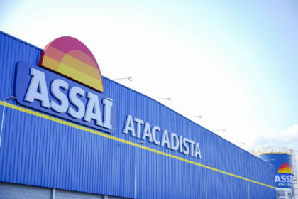 Irmãos Muffato adquirem ações do Assaí através de fundos Fachada azul do supermercado Assaí Atacadista com o logotipo colorido em destaque. Céu claro ao fundo.