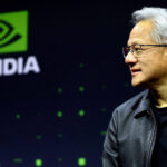 Homem de cabelos grisalhos e óculos, vestindo jaqueta preta, olha para a direita em frente a tela com o logotipo verde e branco da Nvidia.