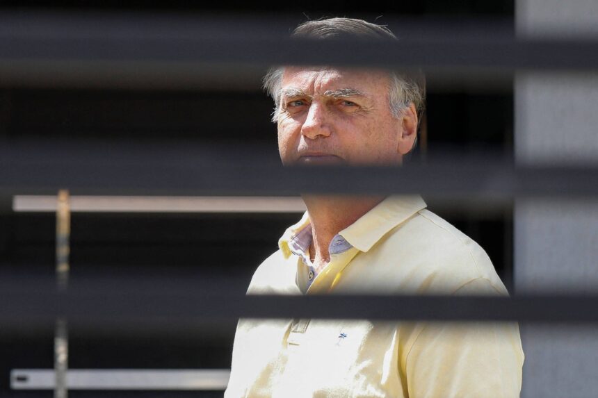 Contestação da base para prisão de Bolsonaro por Moraes Homem de meia-idade com camisa polo amarela observa à frente, enquadrado por persianas horizontais pretas que criam faixas escuras na imagem.