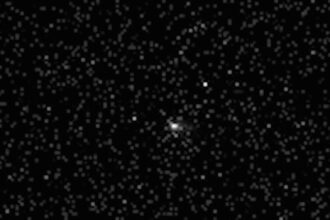 black and white photo of a comet, seen as a blurry white orb, in deep space, with fuzzy and distant stars all around