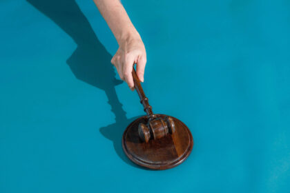 Justice do RJ mantém afastamento de diretoria da Oi até janeiro Mão segura martelo de juiz de madeira sobre base redonda de madeira, fundo azul.