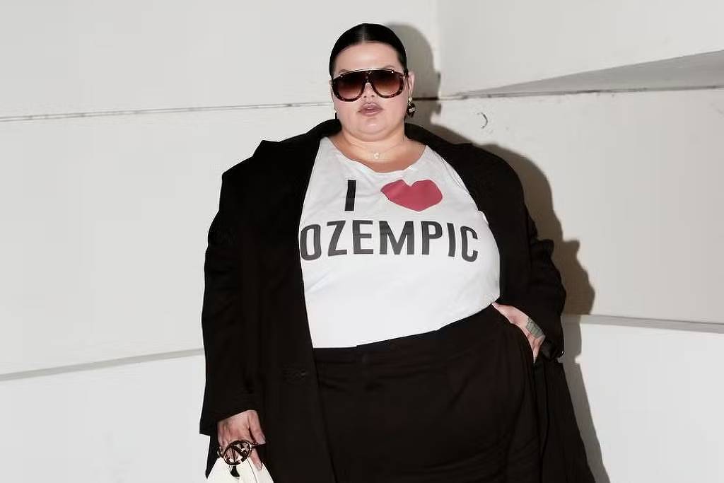 USP avalia uso não autorizado de canetas para emagrecimento A imagem mostra uma mulher posando em um ambiente interno. Ela está vestindo uma camiseta branca com a frase