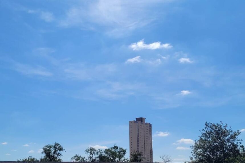 São Paulo registra 35°C e chuvas na segunda-feira Céu azul claro com poucas nuvens brancas dispersas acima de telhados residenciais e árvores. Um prédio alto aparece ao fundo, sob luz do dia clara.