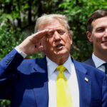 Ex-presidente dos Estados Unidos em terno azul e gravata amarela faz saudação com a mão direita na testa. Homem ao lado veste terno escuro e camisa branca, sorrindo. Fundo com vegetação e luz solar.