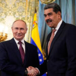 Maduro busca exílio em Belarus enquanto Rússia se mantêm cautelosa Vladimir Putin e Nicolás Maduro apertam as mãos em sala oficial com bandeiras da Venezuela e Rússia ao fundo. Militar observa ao lado.