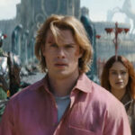 He-Man: assista ao trailer do filme que chega em junho Homem de cabelo loiro e camisa rosa está no centro da imagem, com mulher de cabelo longo e escuro atrás dele à direita. À esquerda, dois personagens com armaduras futuristas e um tigre com listras verdes e amarelas está à direita. Cenário ao fundo inclui estruturas e estátuas em ambiente aberto.