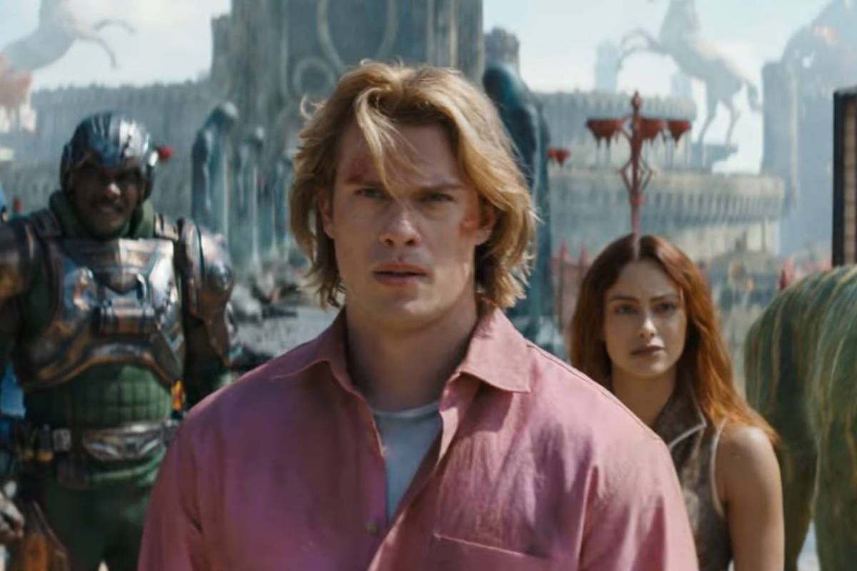 Homem de cabelo loiro e camisa rosa está no centro da imagem, com mulher de cabelo longo e escuro atrás dele à direita. À esquerda, dois personagens com armaduras futuristas e um tigre com listras verdes e amarelas está à direita. Cenário ao fundo inclui estruturas e estátuas em ambiente aberto.